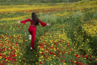 Happy woman wearing red dress running in the field in spring. Spring time blooming flowers