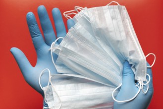 Doctor holds respiratory surgical face mask in hands blue medical gloves on red background.