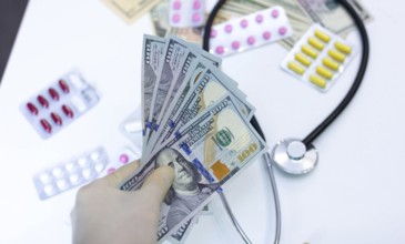 Hand with cash, stethoscope, and pills, illustrating high cost of healthcare