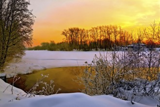 Water and ice on the river, shrubs and trees, wooden house on a background of sunset sky