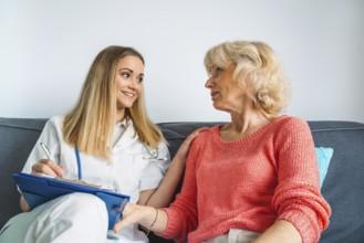 Young blonde woman caregiver helping senior woman at home. Nurse assisting her old woman patient at