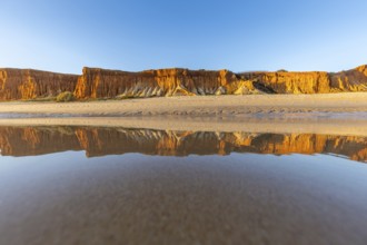 A landscape on the beach at low tide. The surrounding rocks and cliffs are reflected in the sea at