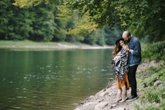 Man hugs a pregnant woman by the lake.
