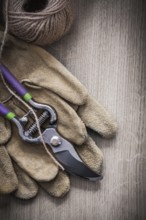 Pair of leather protective gloves sharp metal secateurs and hank of twine on wooden background