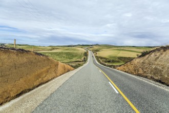 South Island, New Zealand. Incredible cloudy sunset. Great asphalt highway among green fields and