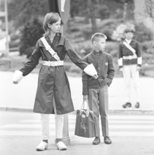 Junior safety patrol in the 1960s. A teenage girl stands with her arms out and signals to the