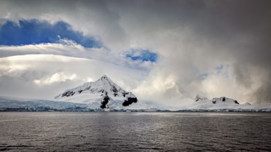 White mountains and clouds are reflected in the dark waters of Antarctica, The coast and landscape