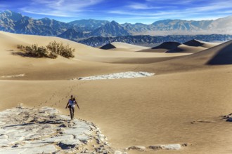 Elderly woman with a camera and a tripod goes among the dunes. Light sand waves from the desert