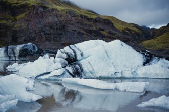 Ice formations near mountains reflecting in calm water under a cloudy sky, iceberg, glacier, snow,
