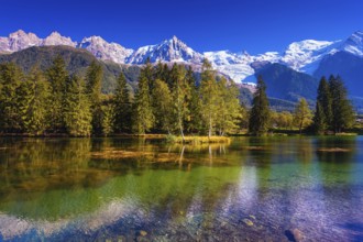 The snow-covered Alps and evergreen fir-trees are reflected in lake. Early fall in Chamonix,