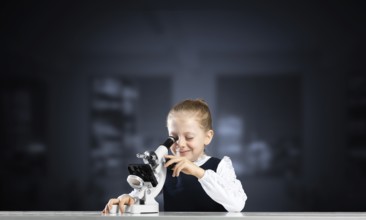 Little girl scientist looking through microscope in classroom at biology lesson. Research and