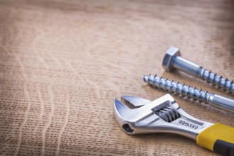 Close up view adjustable wrench and two big screws On Wooden Board