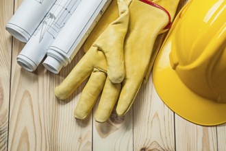 Blueprints yellow gloves and construction helmet on wood boards