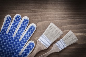 Paintbrushes and protective glove on wooden surface close up view