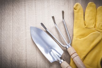 Stainless gardening trowel fork with hand spade and leather safety gloves on wooden board