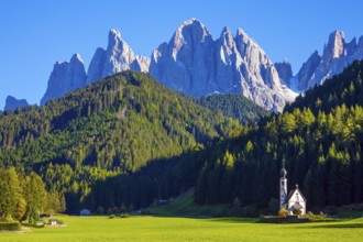 Small white church with among green lawns on the sunset. The village Santa Maddalena in the Val di