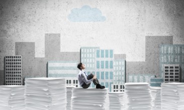 Thoughtful businessman looking away while sitting on pile of documents with drawn cityscape on
