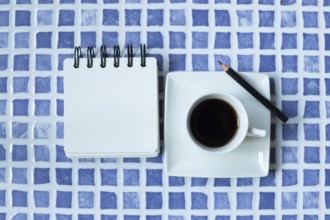 Blank white notepad and cup of coffee on blue ceramic mosaic table. top view, copy space