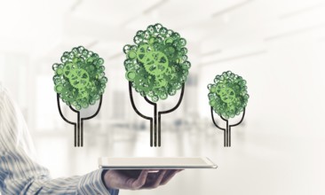 Close of businessman holding tablet pc with green tree made of gears and cogwheels. Mixed media
