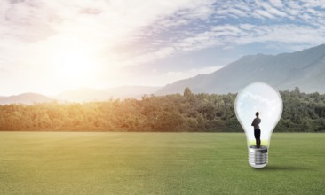 Young businesswoman trapped inside of light bulb on green field
