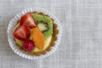 A cake with cream and mixed fruit, resting on linen tablecloth