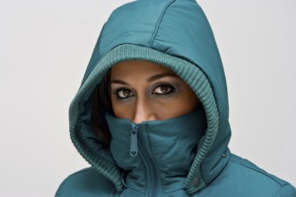 A young woman wearing a green winter coat using the hood to cover her head so that only her eyes