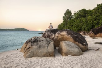 Young Man Meditating and doing Yoga Exercises against beautiful ocean view on stones