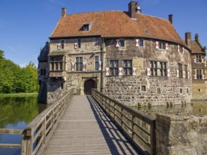 Historic castle with striking wooden bridge and tiled roof, surrounded by moat and blue sky,