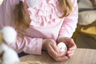 A cute girl with pink bunny ears makes an Easter craft, decorates an egg in the form of a unicorn