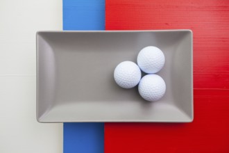 Gray ceramic dish with golf equipments on over white, blue and red wooden table, rectangle dish
