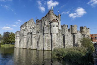 Stone walls of medieval Gravensteen Castle and moat with blue sky, Ghent, East Flanders, Belgium