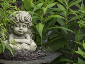 Angel figure made of stone embedded in a nest, surrounded by green plants, borken, münsterland,