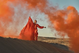 Woman in red dress dancing in the desert at blue sky