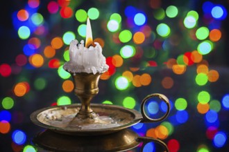 Glowing old candle in wintage candlestick on surface of mirror with multycolored bokeh horizontal