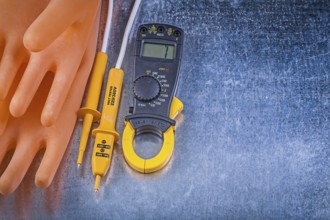 Digital clamp meter electrical tester insulating rubber gloves on metallic background