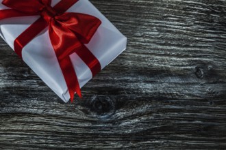 White present box with red bow on wooden board