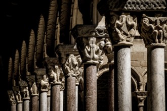 Medieval stone columns with intricate carvings and arches create a shadowy and ornate architectural