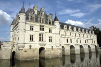 Historic stone castle with turrets and windows, reflected in surrounding water under a blue sky.