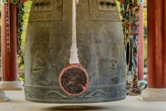 Closeup of bronze bell and striker in pavilion in mountainside Buddhist temple