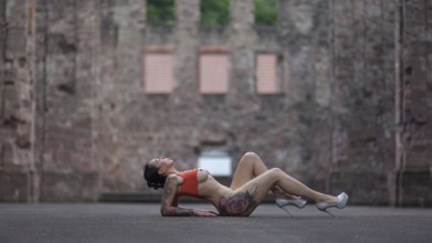 Woman in sporty pose and high heels lying on the ground in front of an old ruin, Staged outdoor
