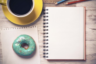 Opened notepad and cup of coffee with donut on wooden table