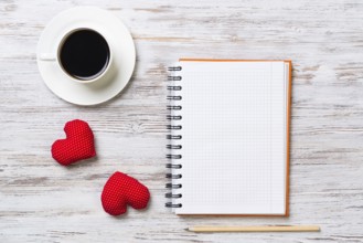 Coffee cup notepad pencil and two red hearts on wooden surface