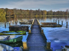 Wooden jetty leading to several boats on a lake with autumn landscape and blue sky, Borken,