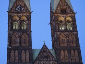 Detailed view of two Gothic church towers with clocks, illuminated in the soft evening mood,