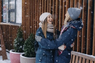 Erwachsene Freundinnen, die sich umarmen und lachen und sich über das verschneite, kalte Wetter