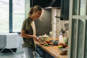Eine junge, glückliche, blonde, lächelnde Frau, die in einer Küche zu Hause Essen kocht
