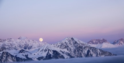 full moon rising into a pink sky in a winter mountain landscape in the Alps of Switzerland