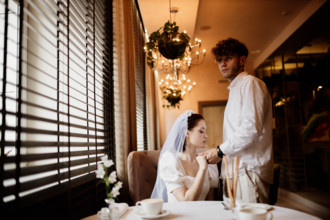 A couple in formal attire shares a tender moment indoors under warm lighting