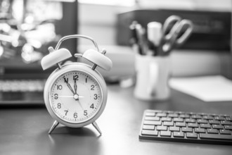 Alarm clock on the desk, office stuff in the blurry background, deadlines and todos