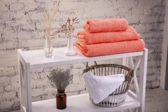 Rack with a stack of three peach colour towels and baskets with clean white towels and toilet decor